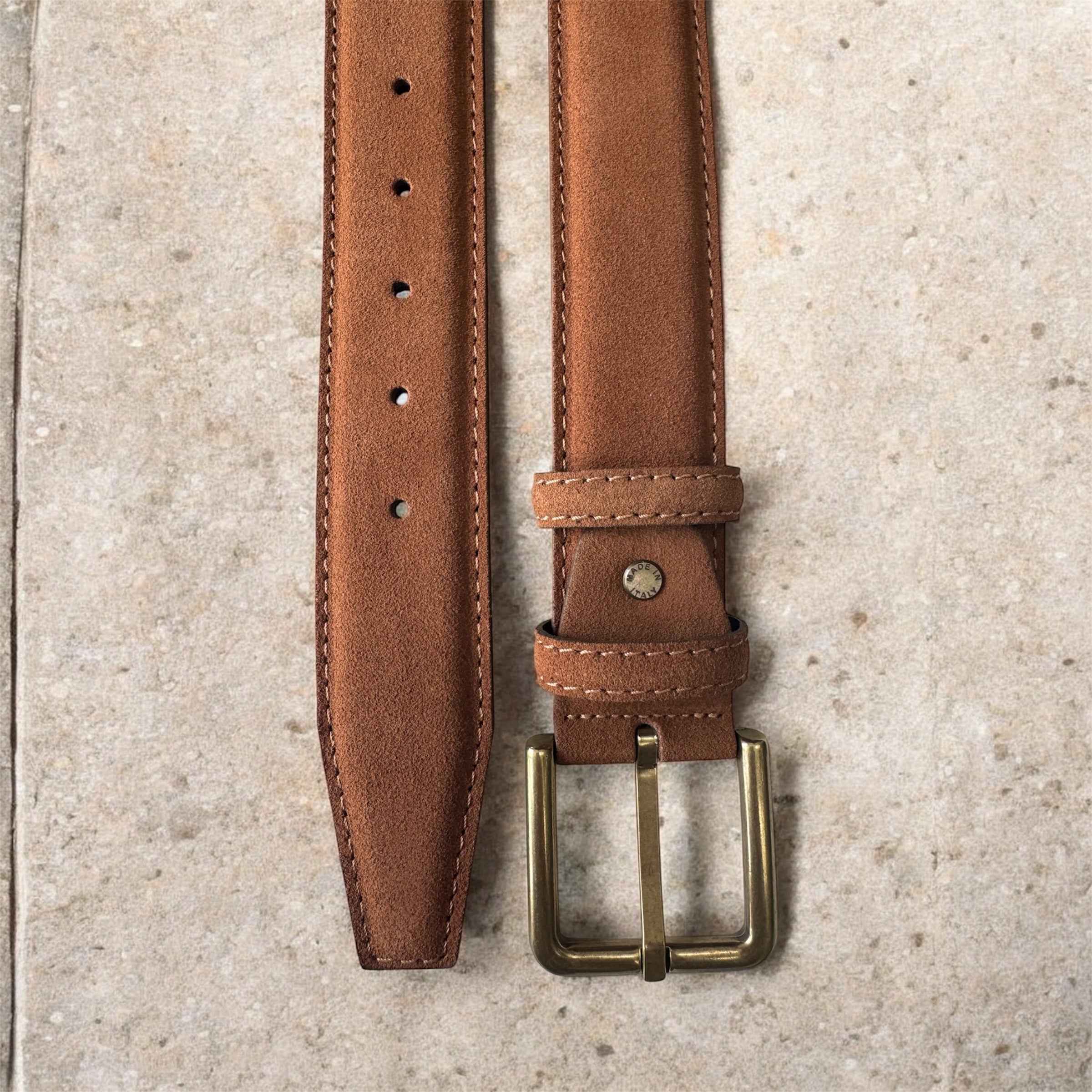 Tan leather belt with brass buckle on a textured surface