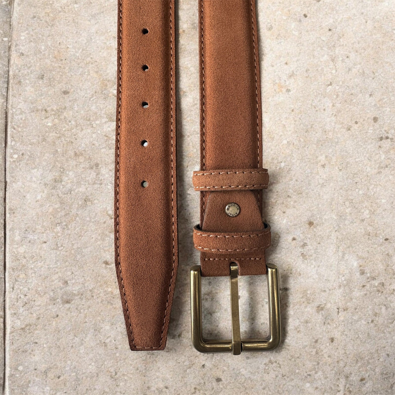 Tan leather belt with brass buckle on a textured surface